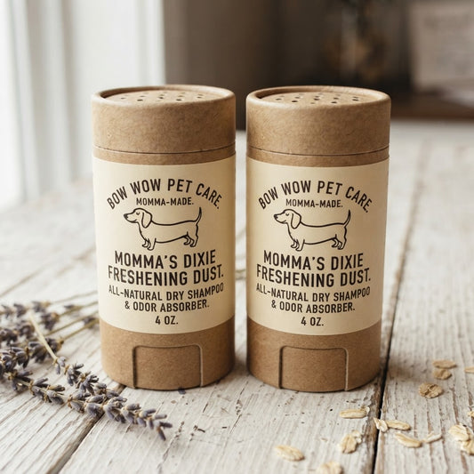 Two cylindrical pet shampoo and odor absorber stick containers labeled 'BOW WOW PET CARE' and 'MOMMA'S DIXIE FRESHENING DUST,' placed on a rustic wooden surface with dried lavender and oat flakes nearby.